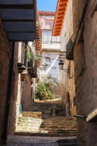 Callejón estrecho con escaleras de piedra y casas tradicionales en el casco histórico de Valderrobres con balcones y vegetación