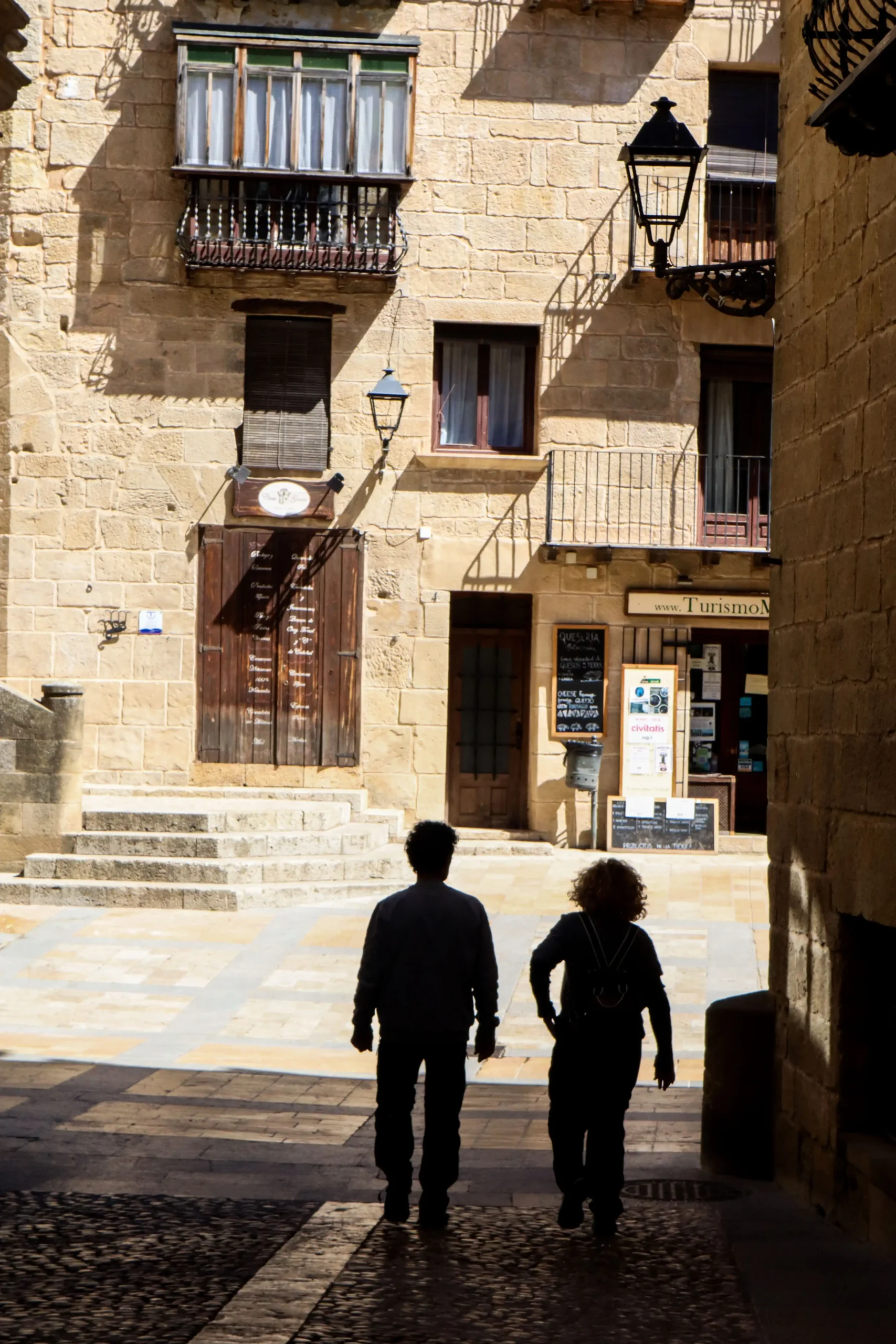 Personas caminando hacia una plaza del casco histórico de Valderrobres con edificios de piedra y arquitectura tradicional