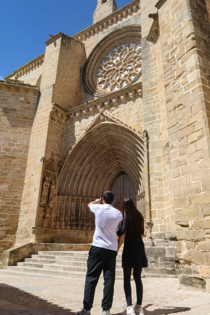 Pareja observando la portada gótica de la Iglesia de Santa María la Mayor de Valderrobres con rosetón y detalles arquitectónicos